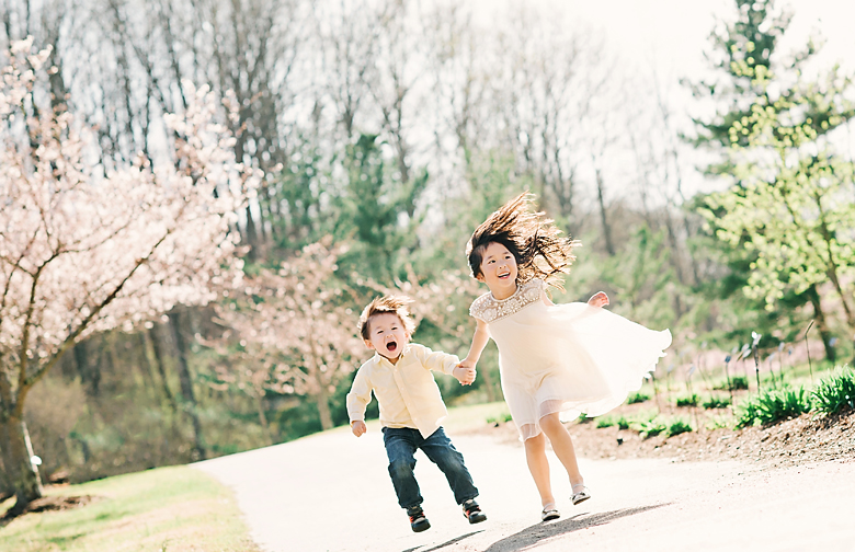The brother and sister joyfully run hand in hand, their hair flying in the sunlight.