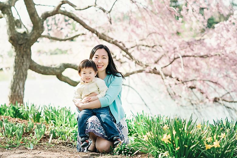 Mom crouching under the cherry blossom tree, holding her son.